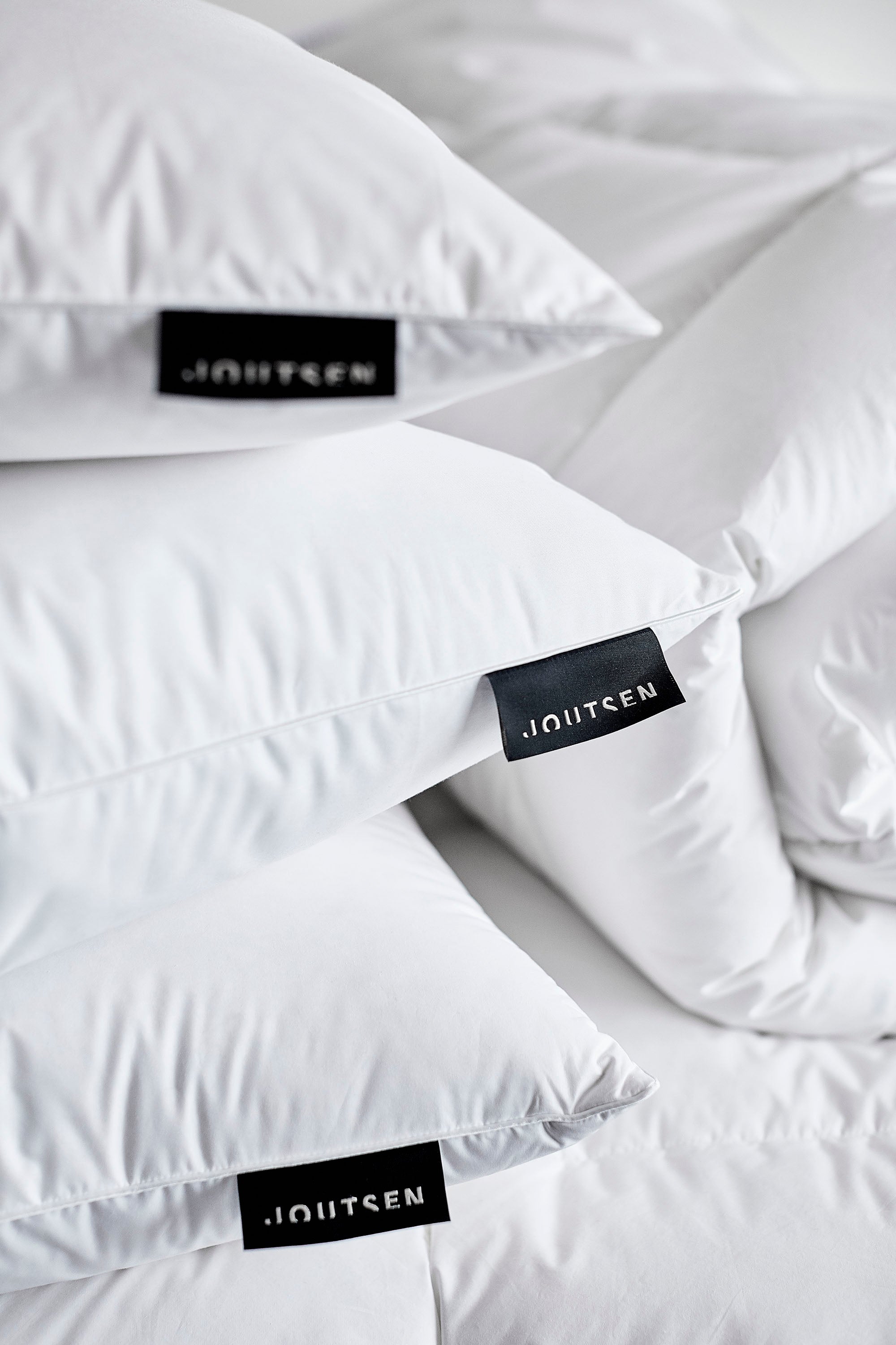 White pillows with Joutsen labels on a white background. here is also a white down duvet rolled behind.