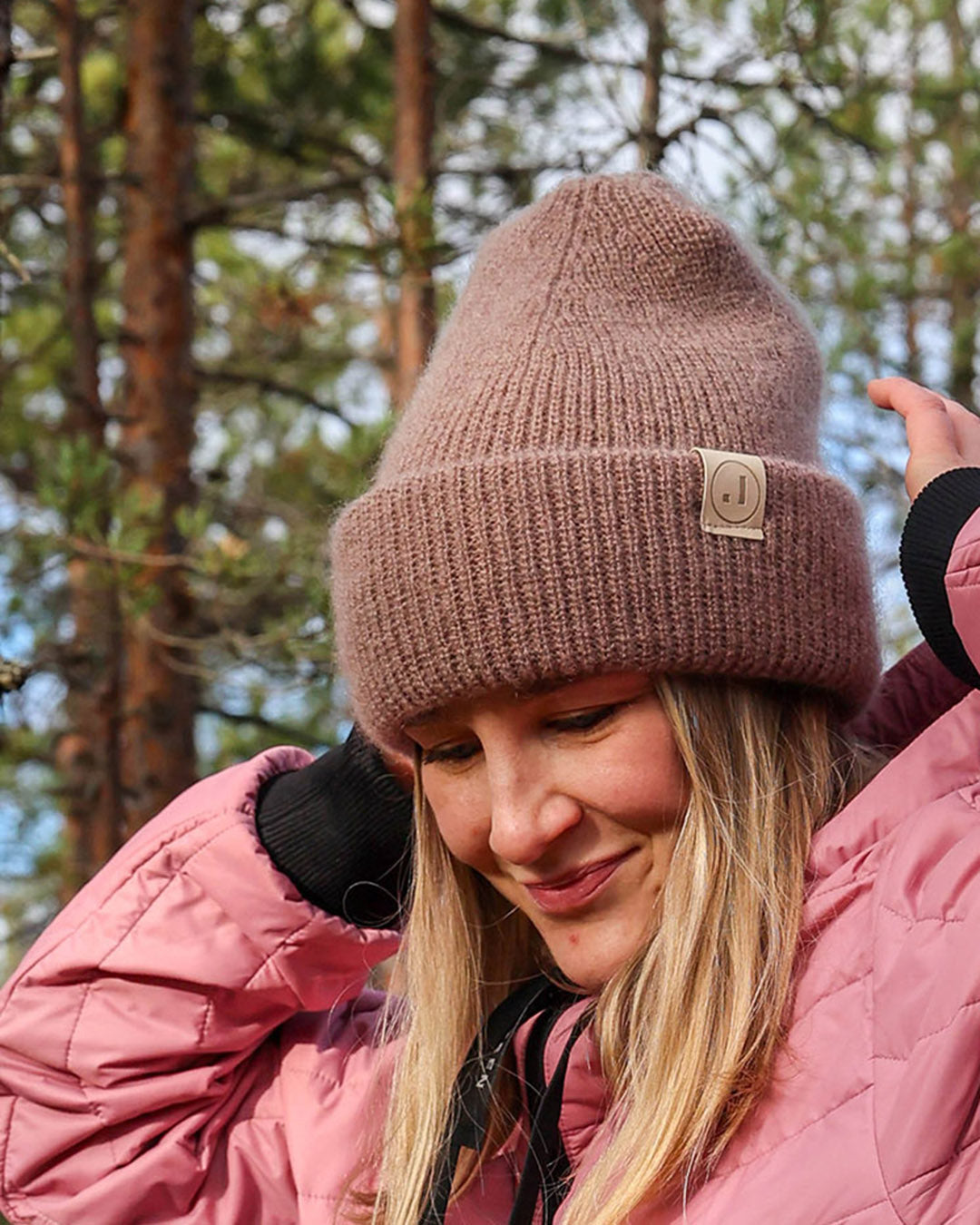 Woman wearing a brown knit beanie and pink jacket in a forest setting