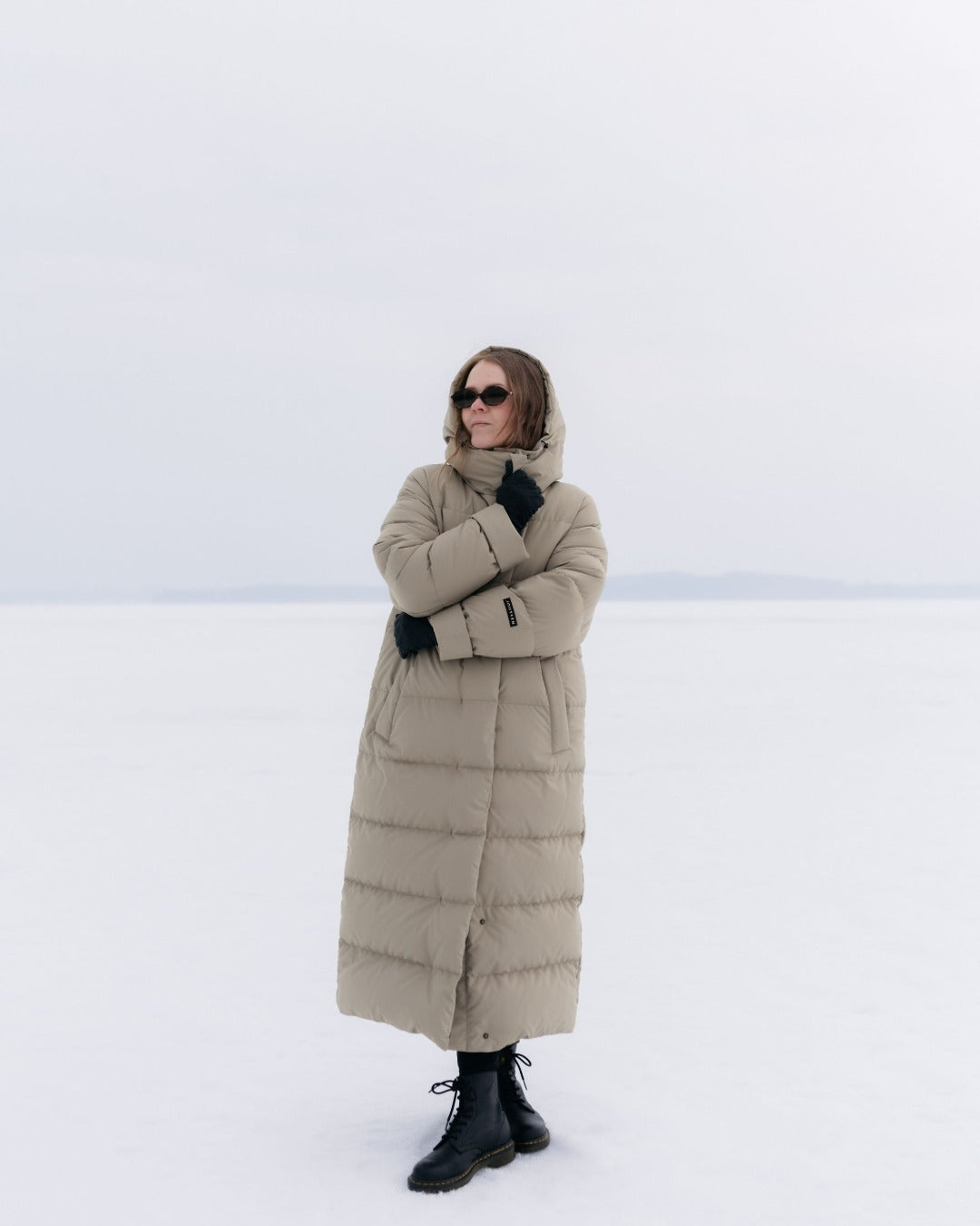 Person wearing a long beige Blenda down coat in a snowy landscape