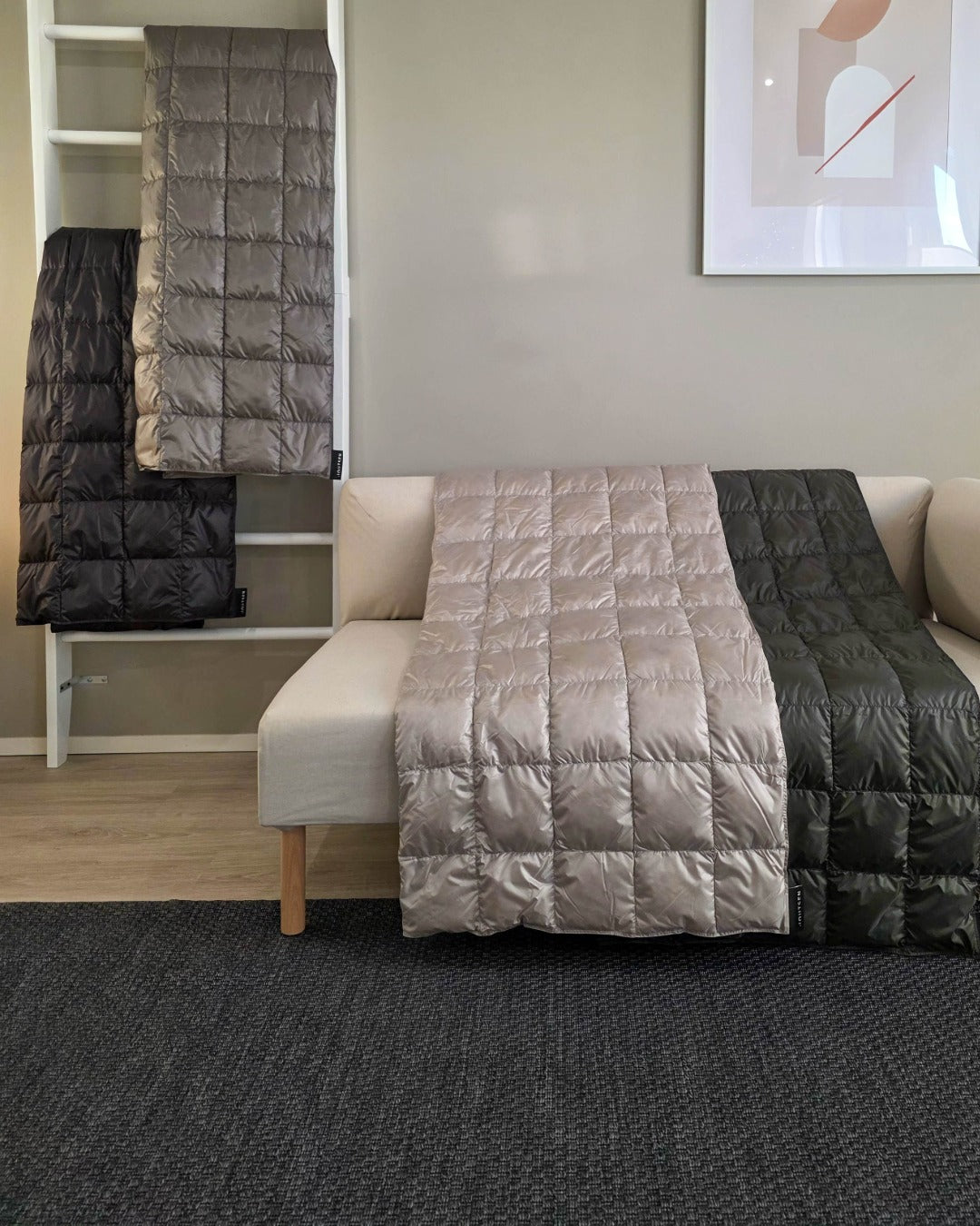 Folded Kulkuri down blankets on a sofa and a chair in a room with a gray rug.