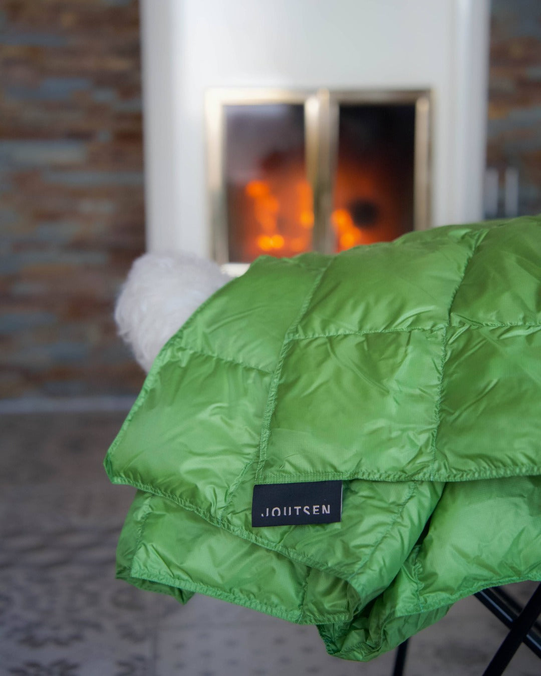 Green Kulkuri down blanket with a brand label in front of a fireplace.