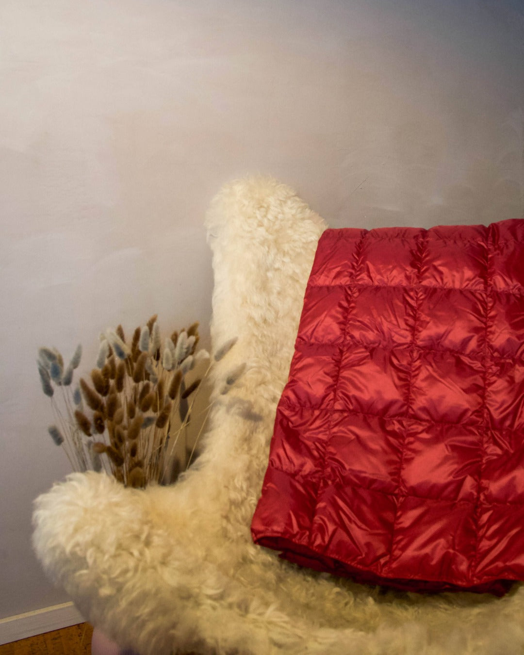 Red Kulkuri down blanket draped over a white fur chair against a plain wall.