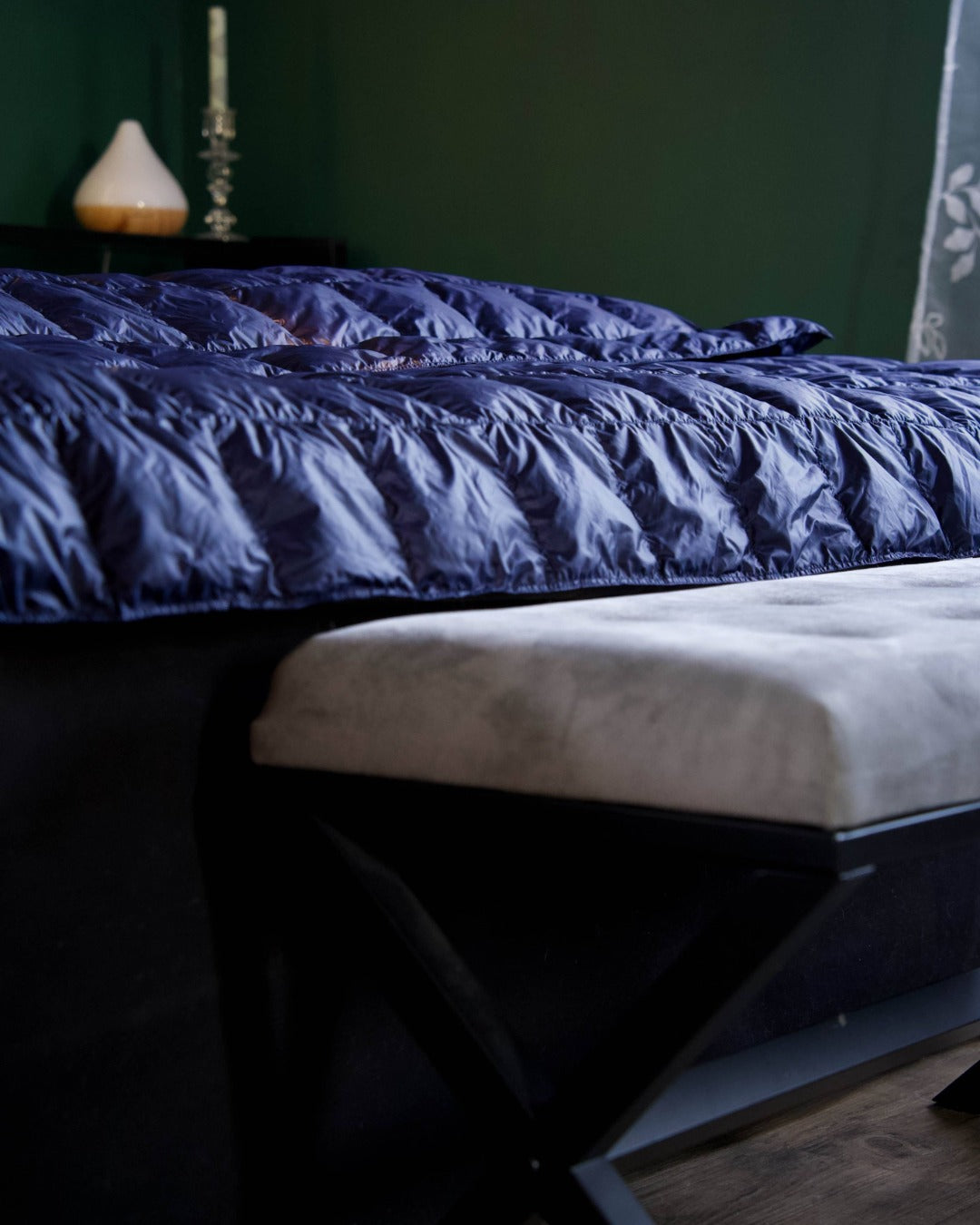 Dark blue down blanket on a bed with a dark green wall in the background