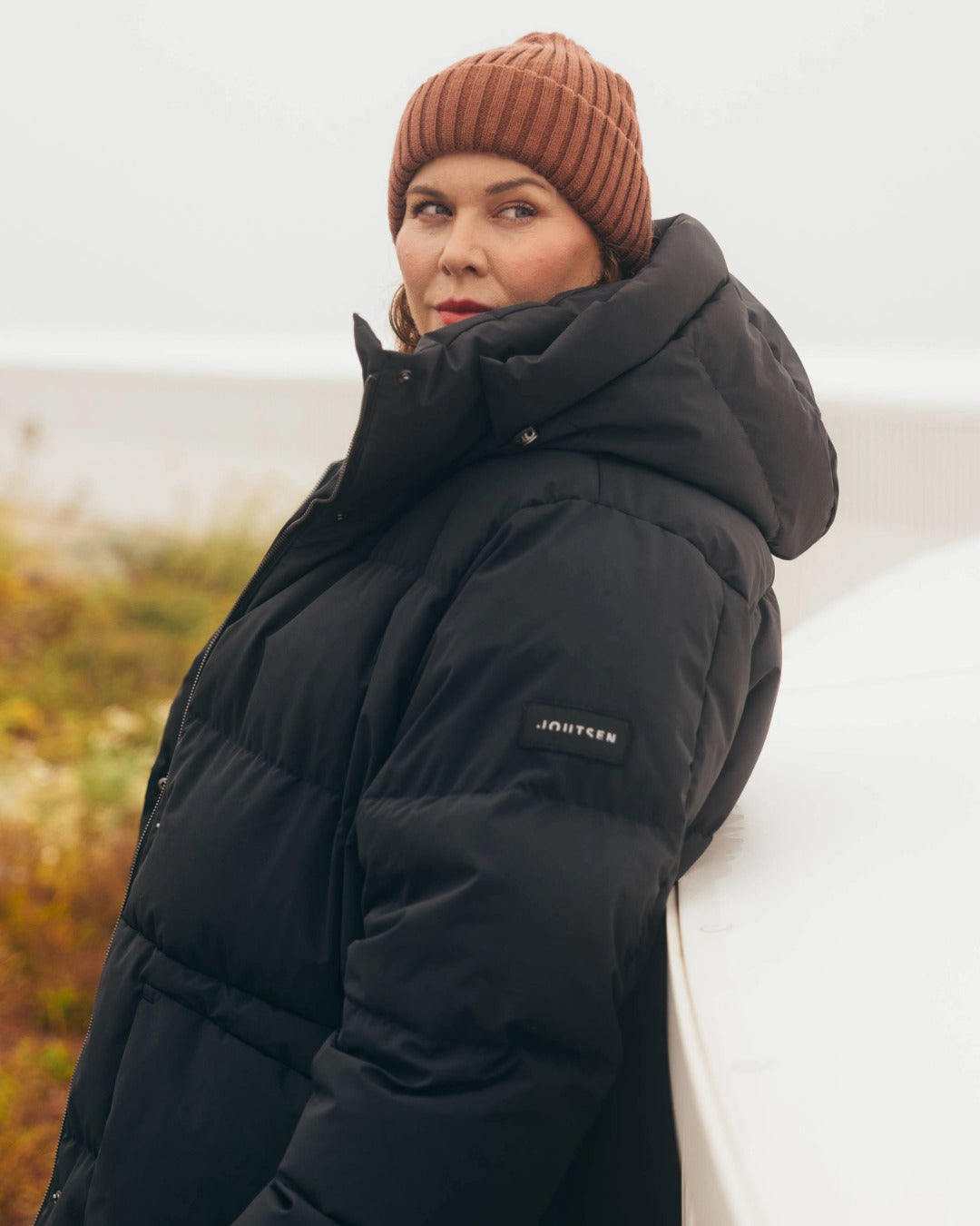 Person wearing a black down coat with a brand logo, standing outdoors.