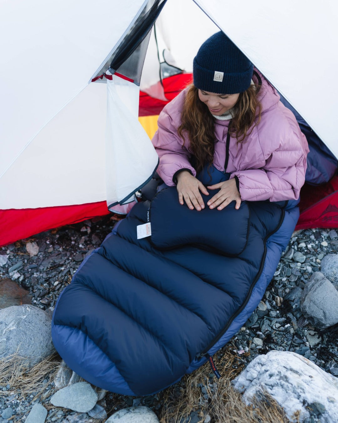 Person using a blue sleeping bag outdoors next to a tent.