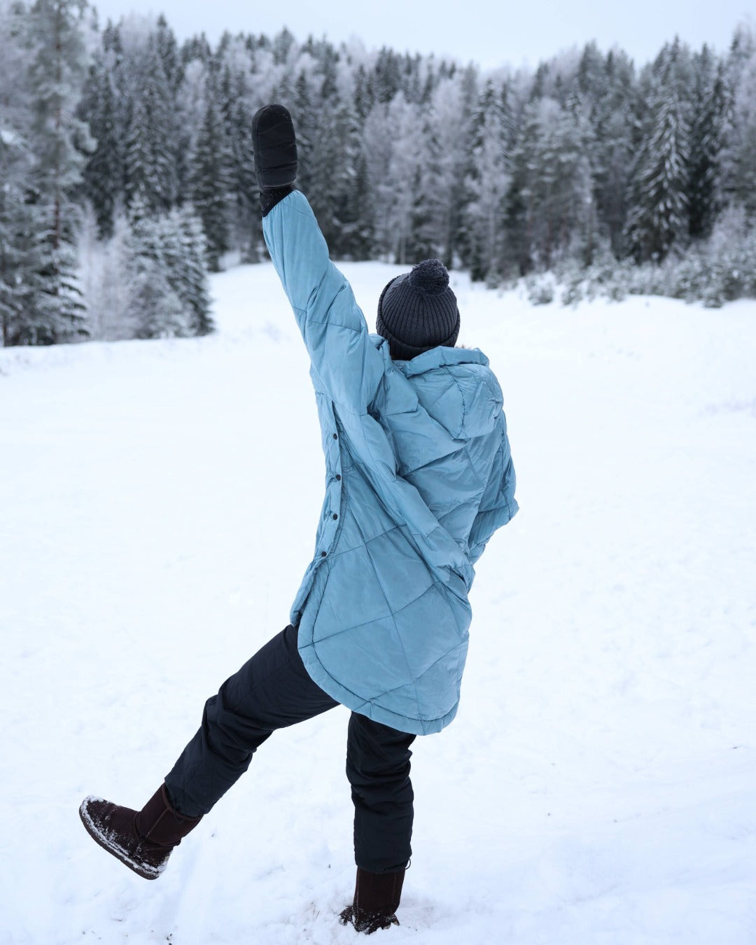Person in a light blue down anorak standing in a snowy landscape with trees in the background