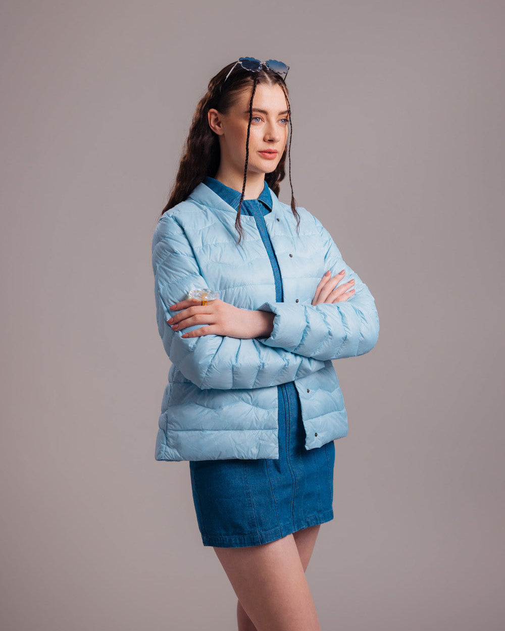 A woman dressed in a light blue horizontally quilted Lootus light down jacket (color: Frozen candy), featuring a straight cut and long sleeves. The jacket is paired with a blue denim dress and sunglasses.