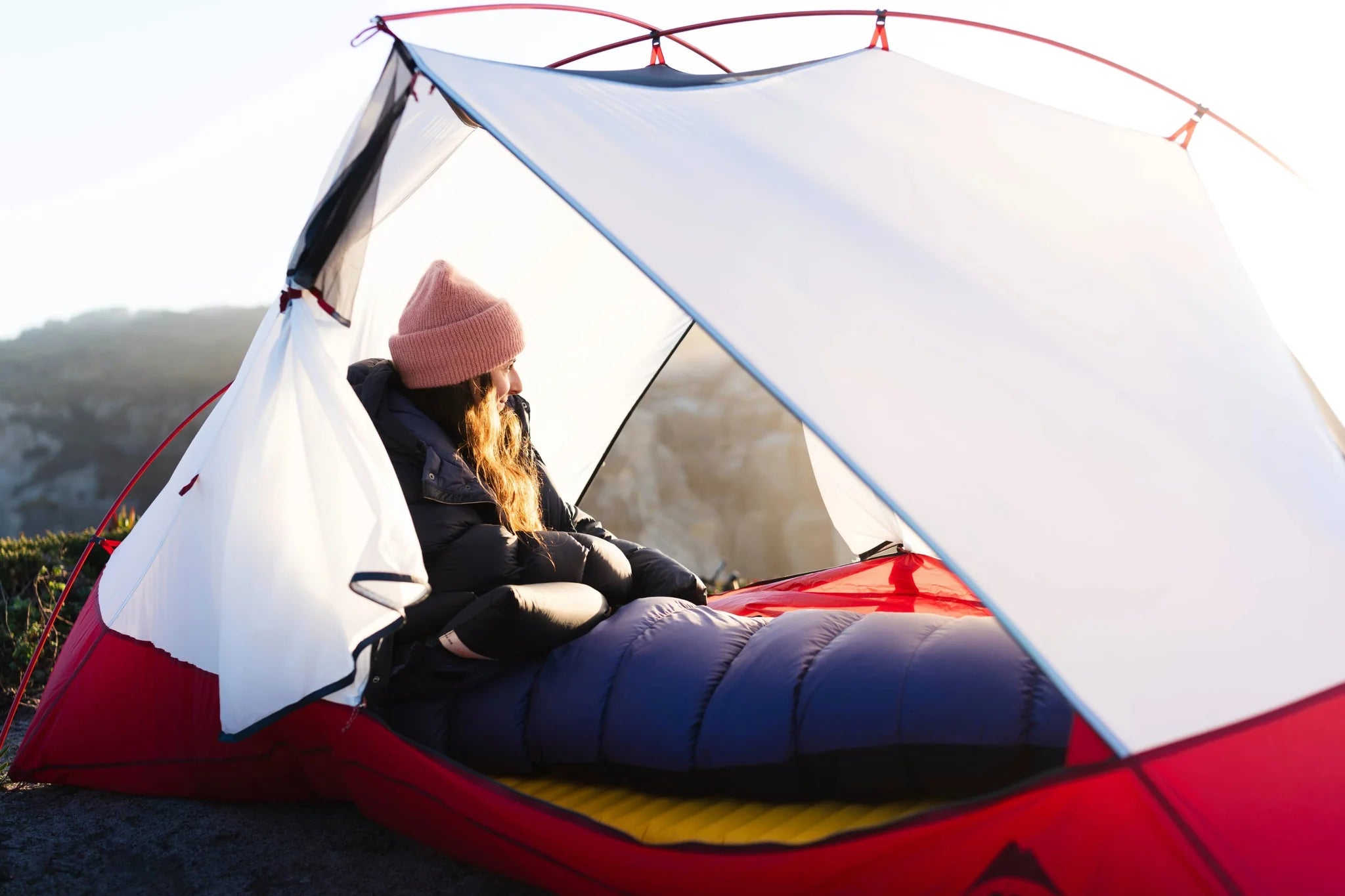 Person sitting inside a red and white tent with a scenic background