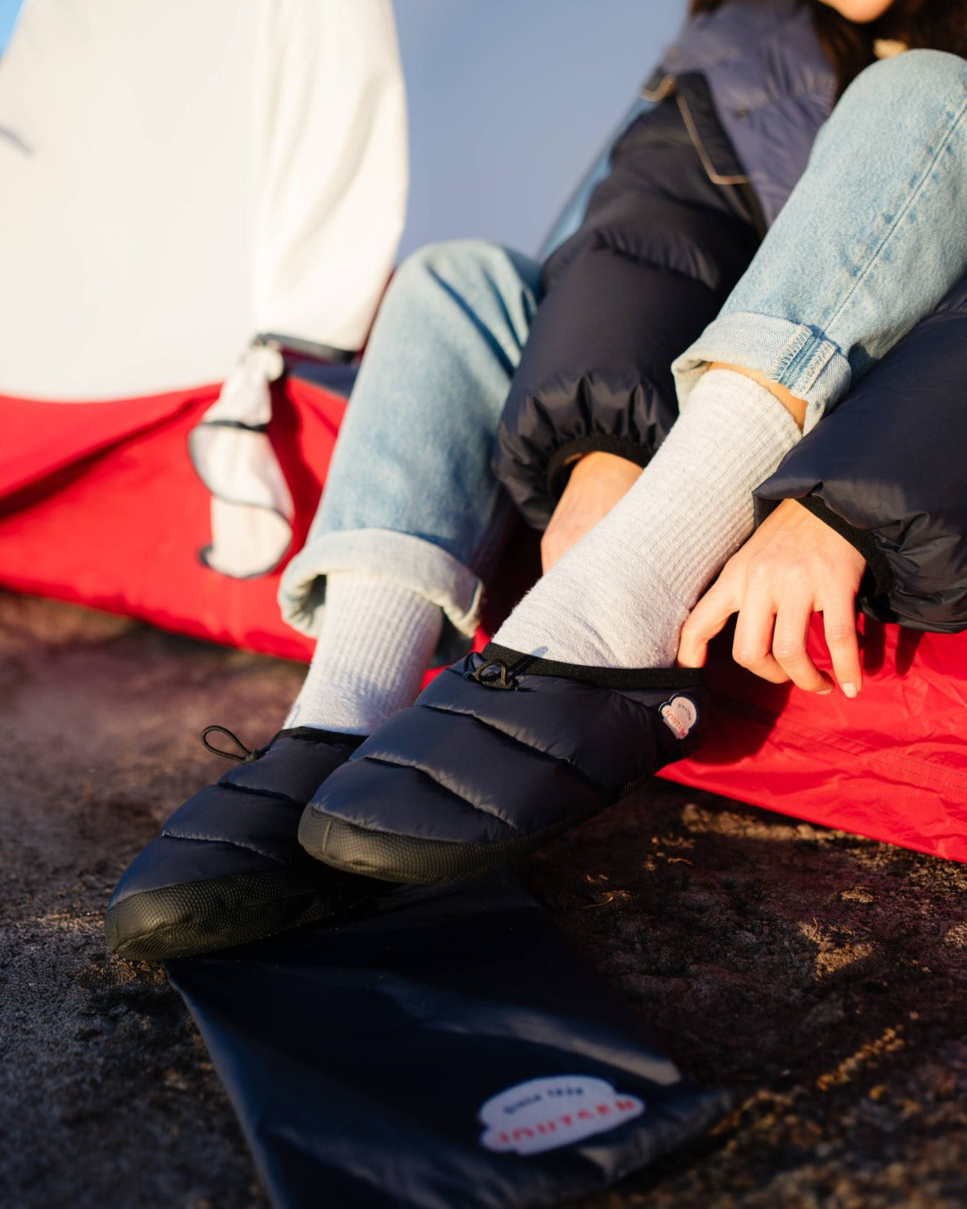 Person wearing black down camp slippers with a visible brand logo