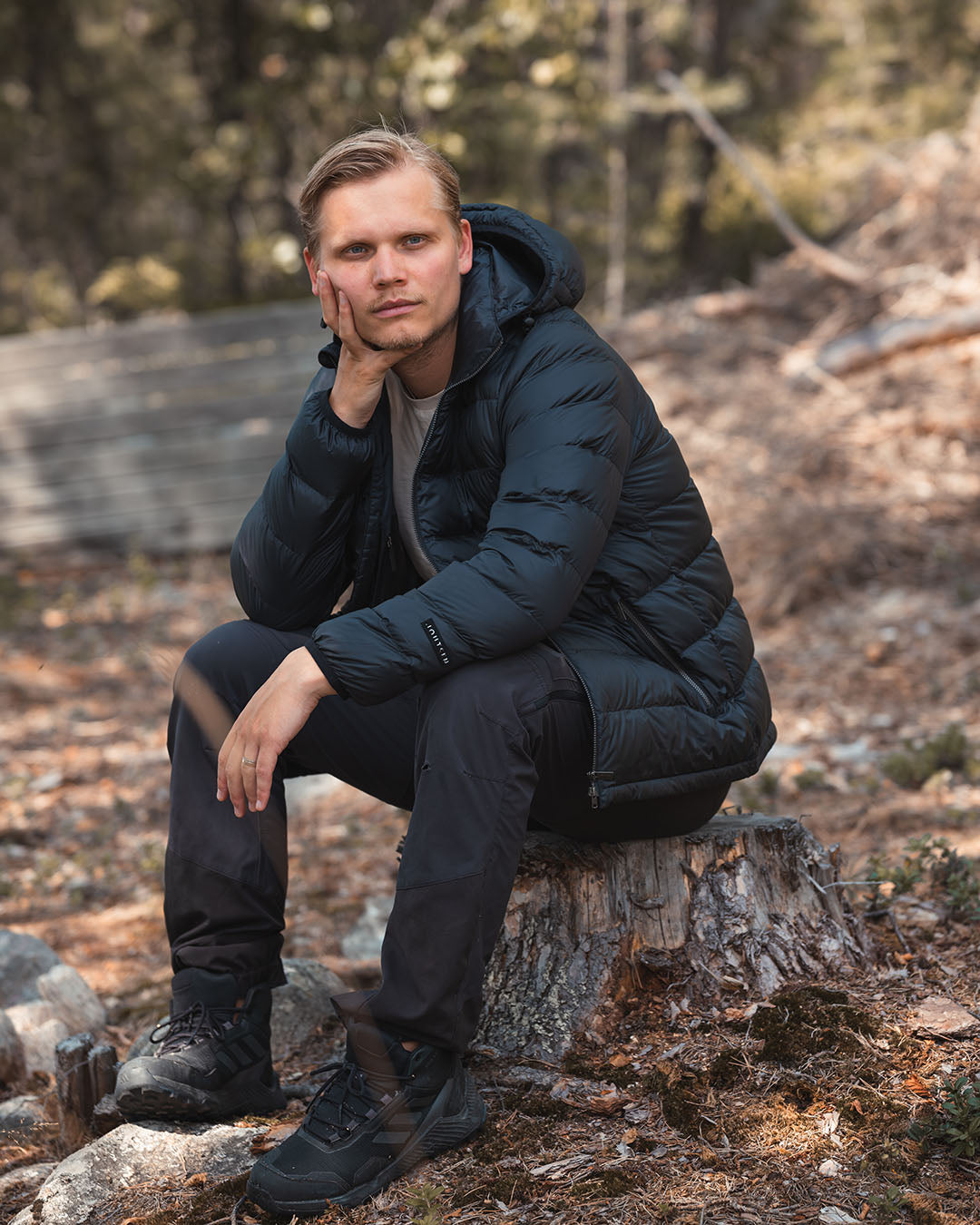 Man sitting on a tree stump in a forest wearing a black light down coat