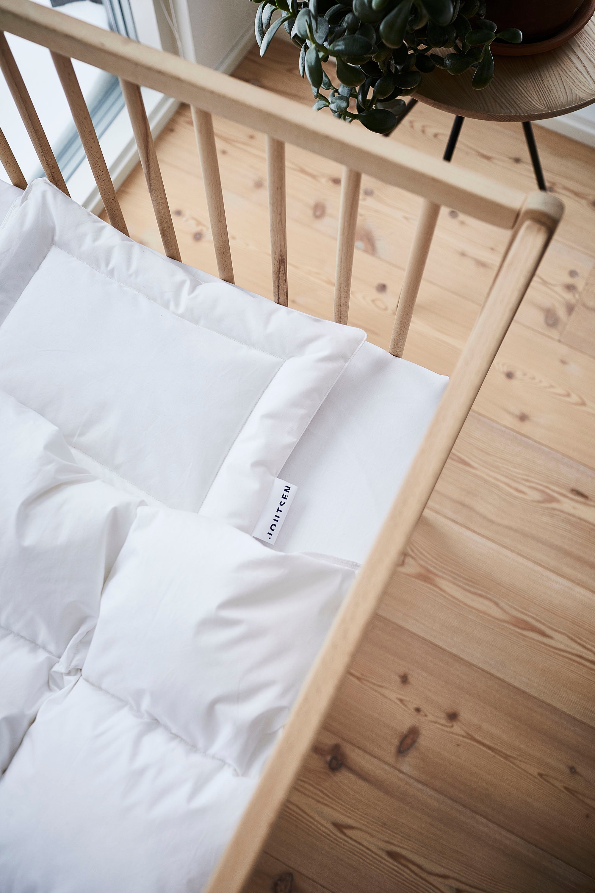 White comforter on a wooden baby bed frame with a plant in the background