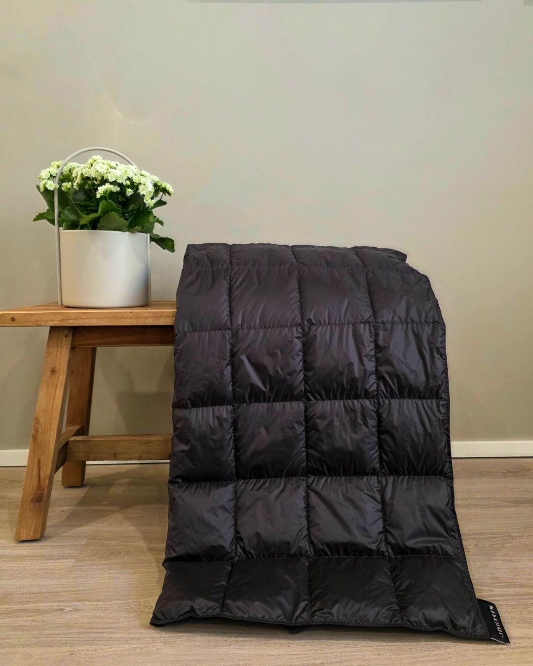 Dark grey Kulkuri down blanket on a wooden floor with a small table and plant in the background.