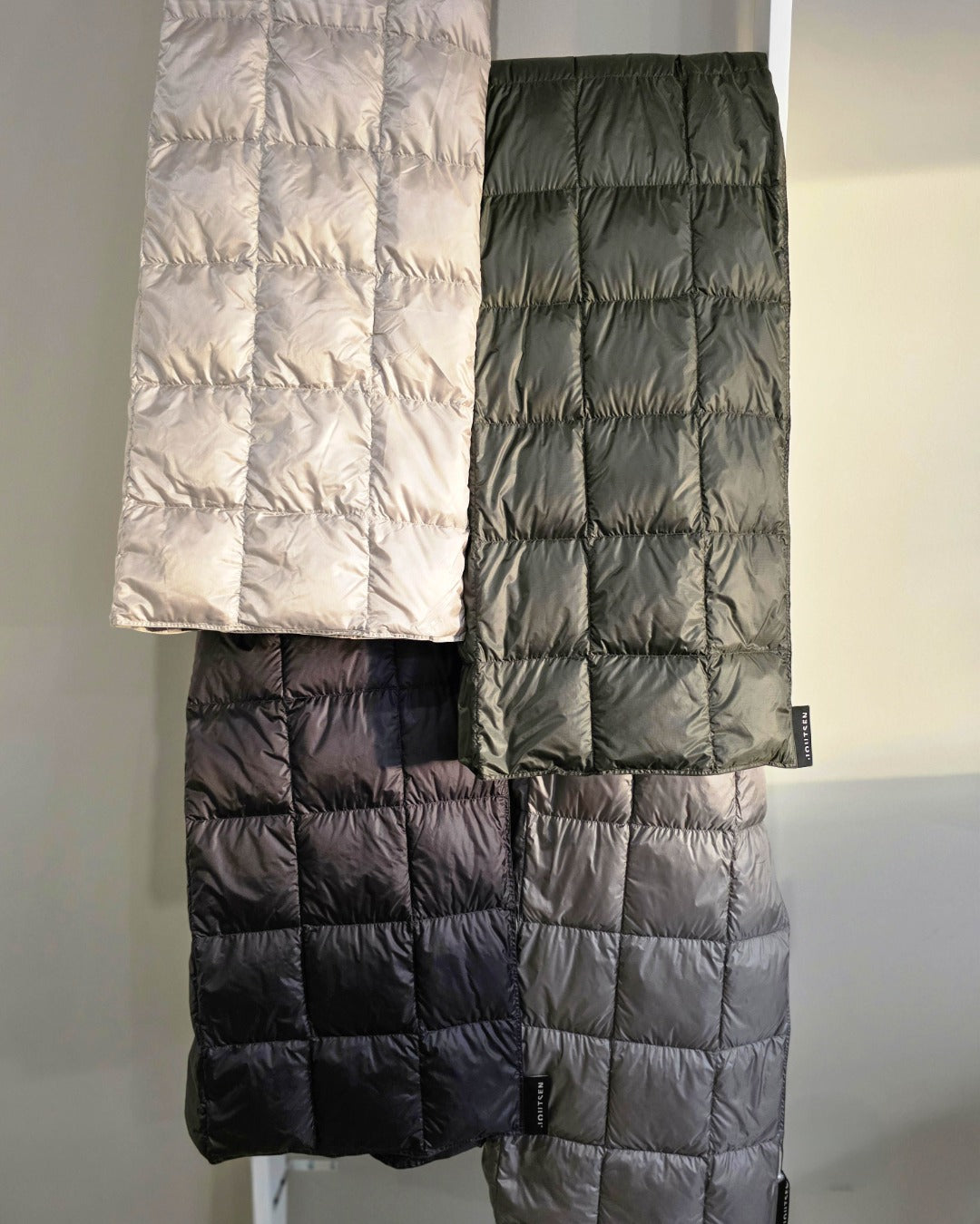 Four Kulkuri down blankets in different colors hanging on a rack.