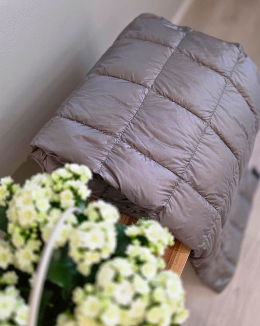 Gray Kulkuri down blanket on a wooden surface with white flowers in the foreground