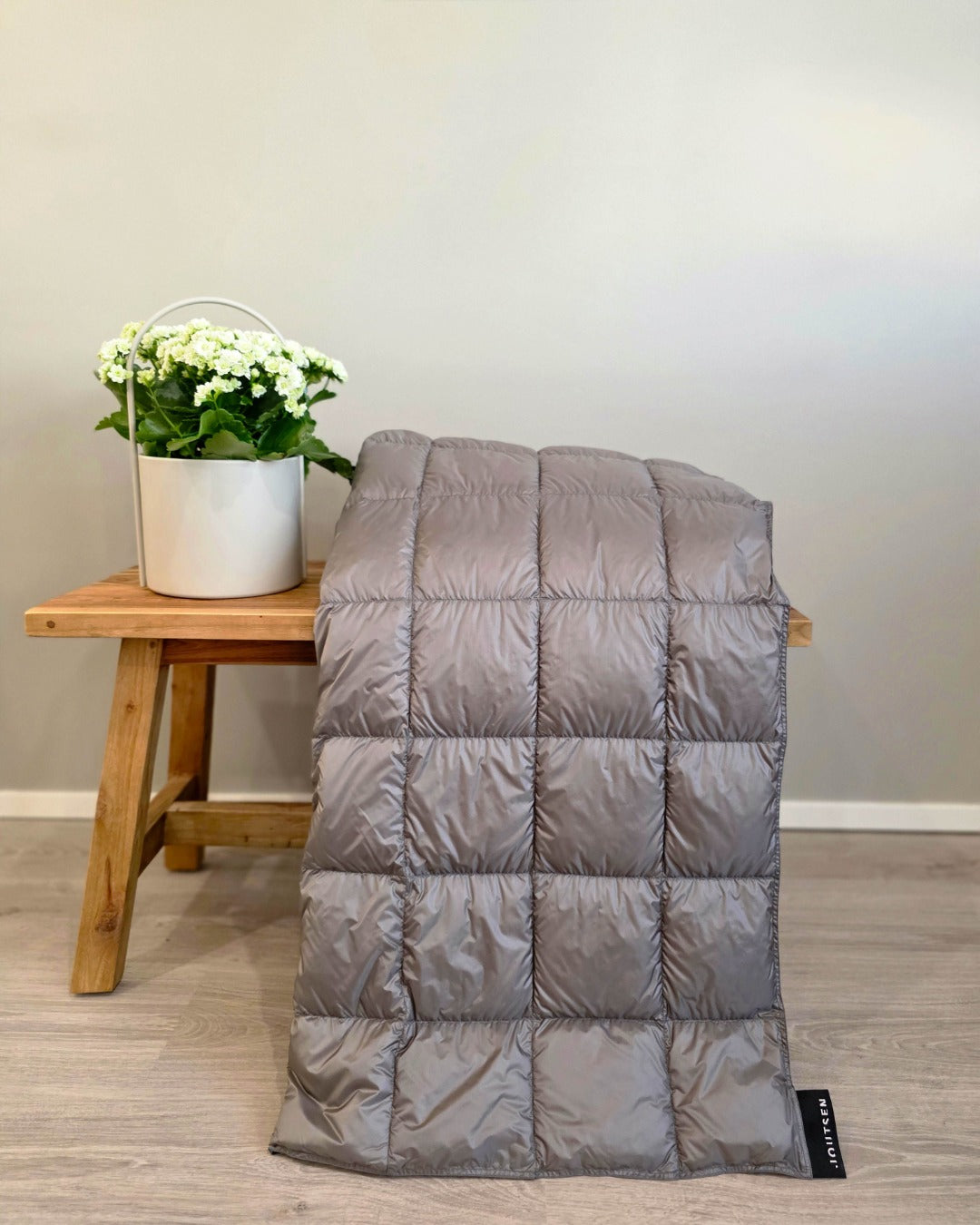 Gray Kulkuri down blanket on a wooden stool with a white bucket of flowers against a plain wall.