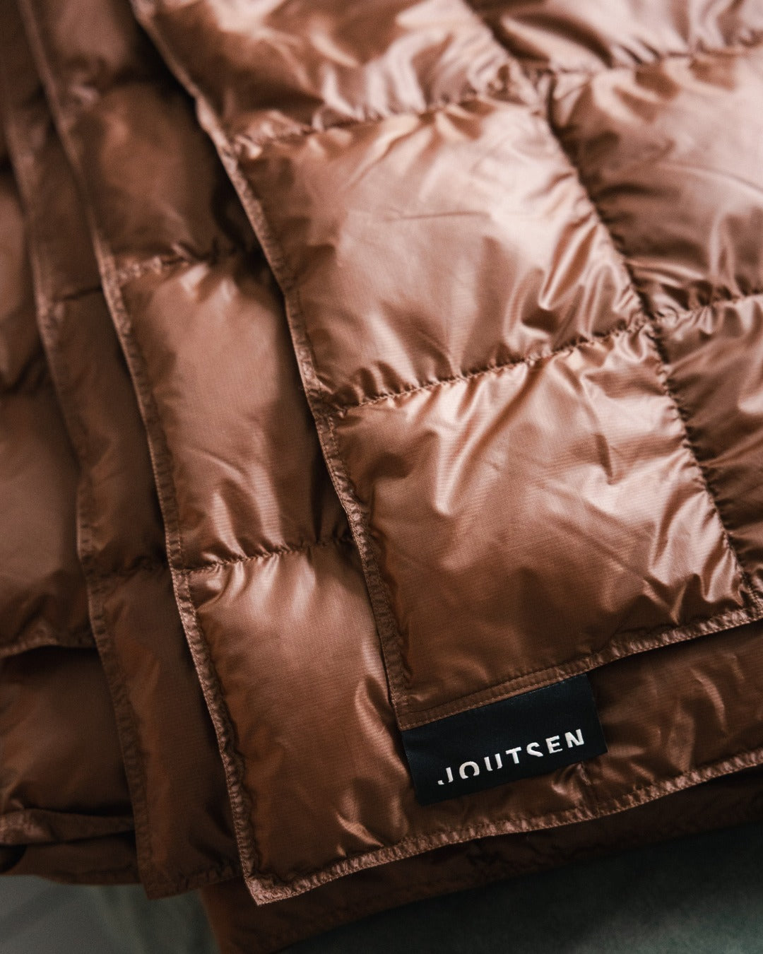 Close-up of a brown (color: chocolate mousse) quilted Kulkuri down blanket with 'Joutsen' branding.