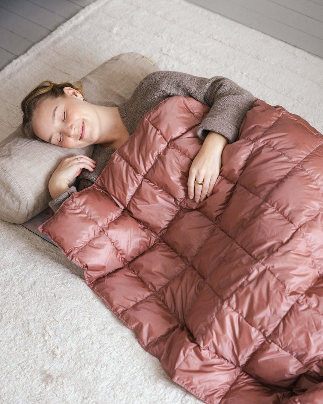 Woman lying on a sofa with a light pink (color: old rose) Kulkuri down blanket.