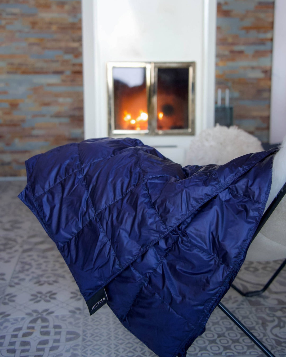 Blue Kulkuri down blanket on a chair with a fireplace in the background