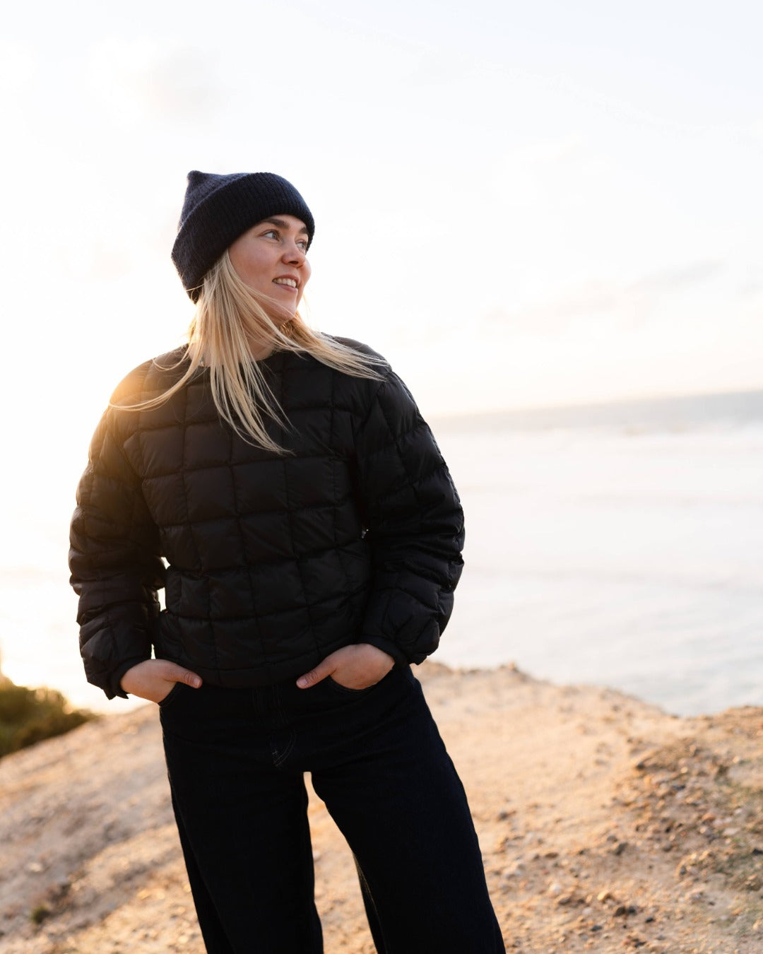 Person wearing a black down college shirt and beanie standing on a beach.