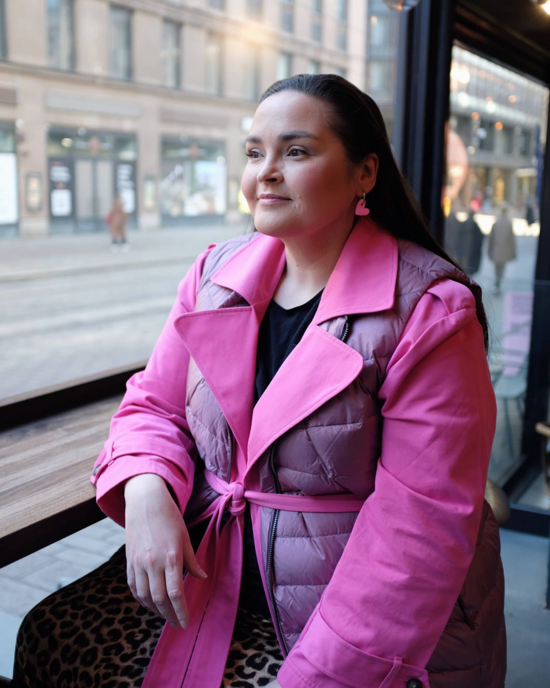 Woman wearing a pink down vest sitting on a train with a cityscape in the background