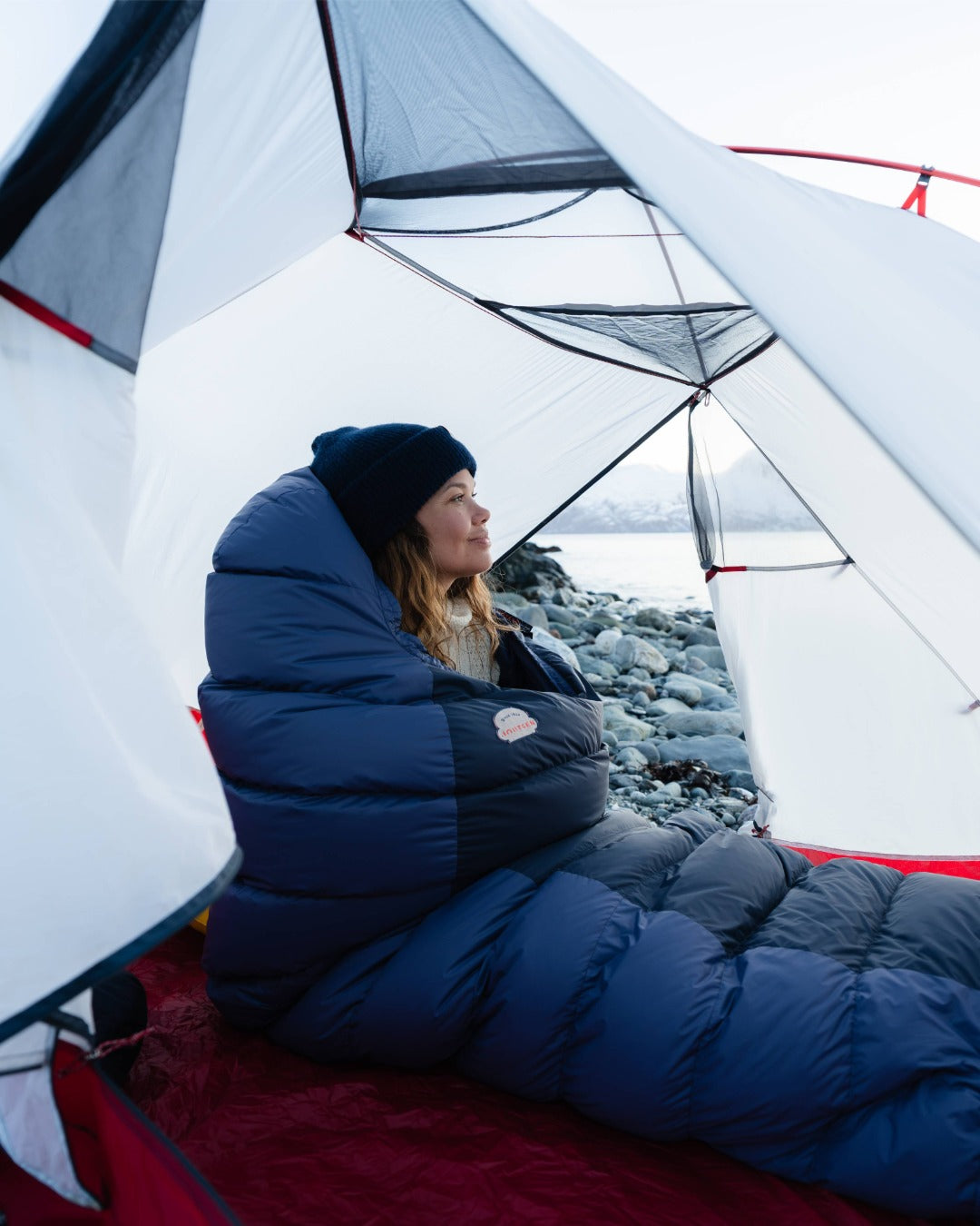 Person in a blue sleeping bag inside a tent with a scenic view outside