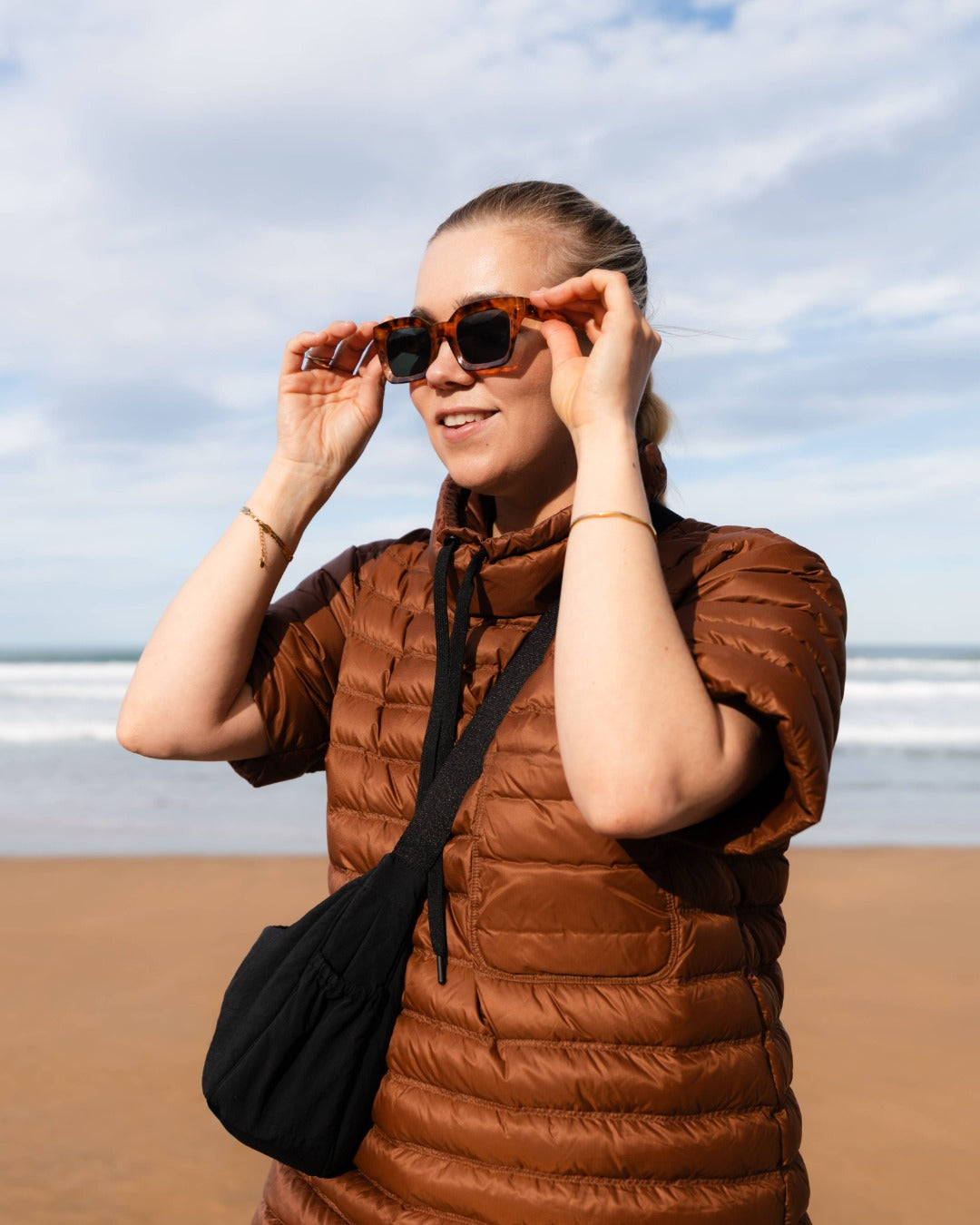 Woman in a brown down shirt and sunglasses on a beach