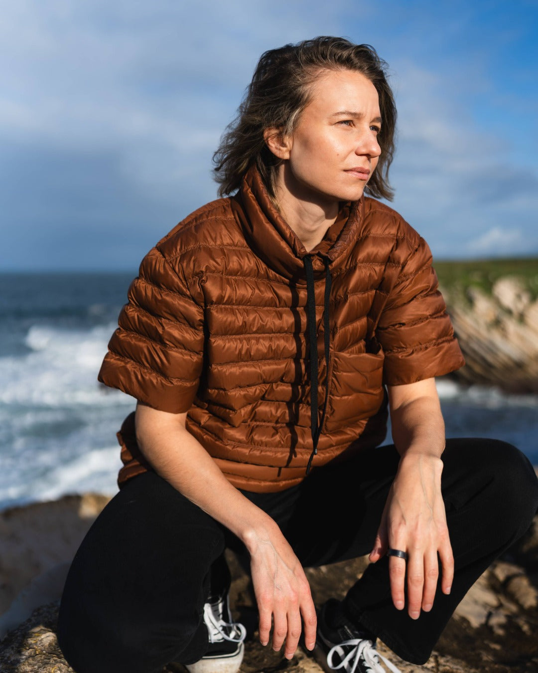 Person wearing a brown down shirt sitting by the ocean