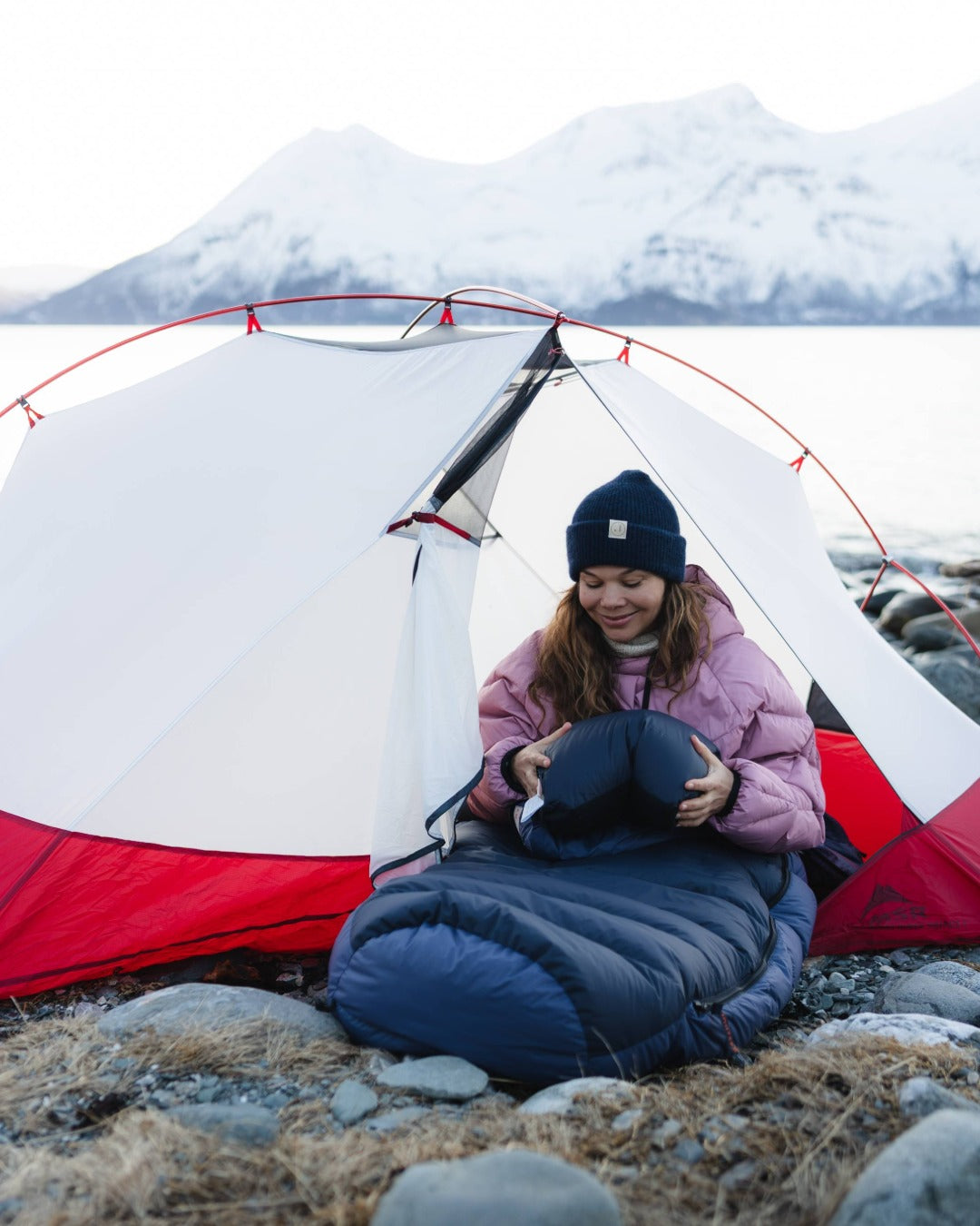 Person sitting inside a red and white tent by a snowy mountain landscape