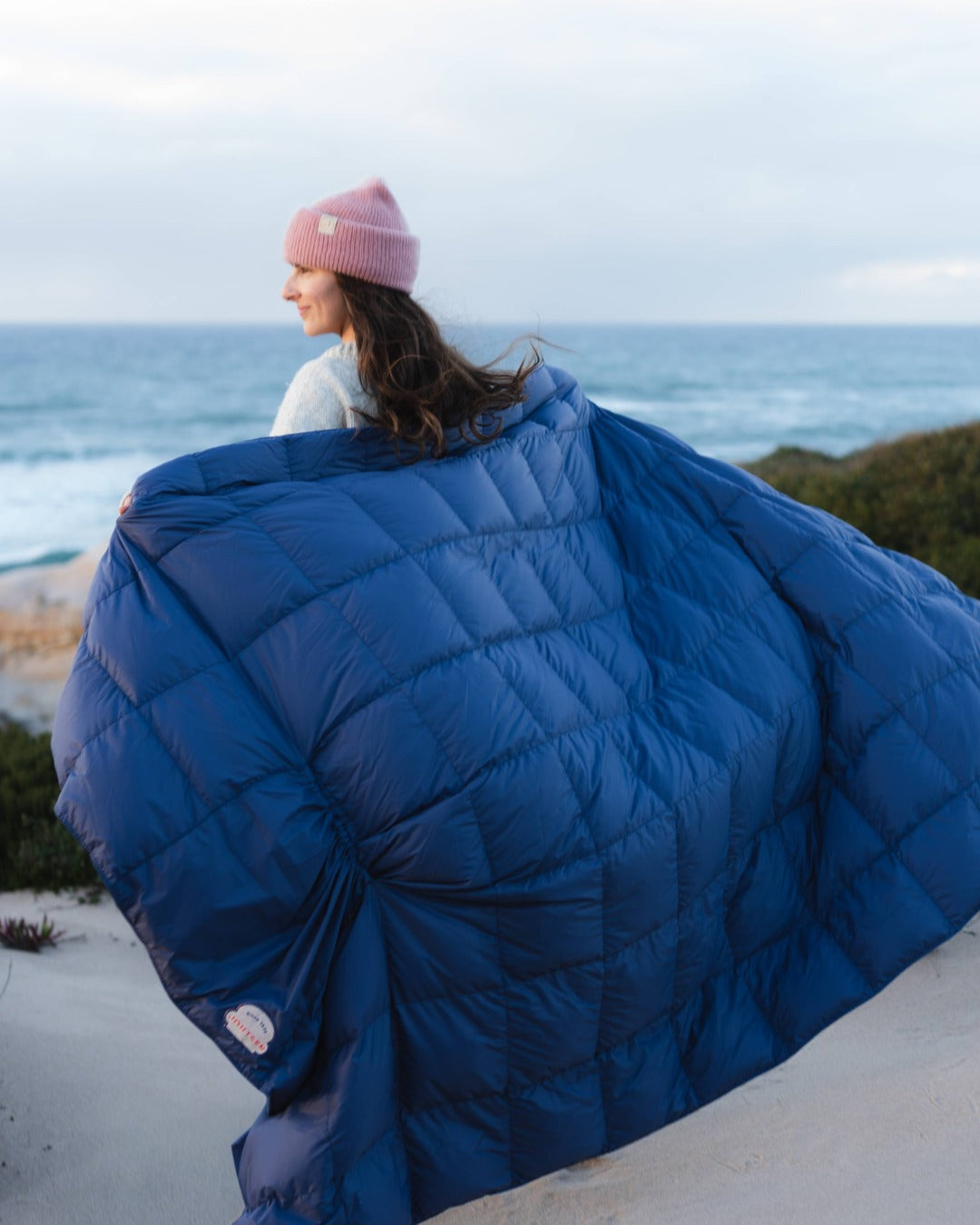 Person wearing a large down blanket on a beach with ocean view