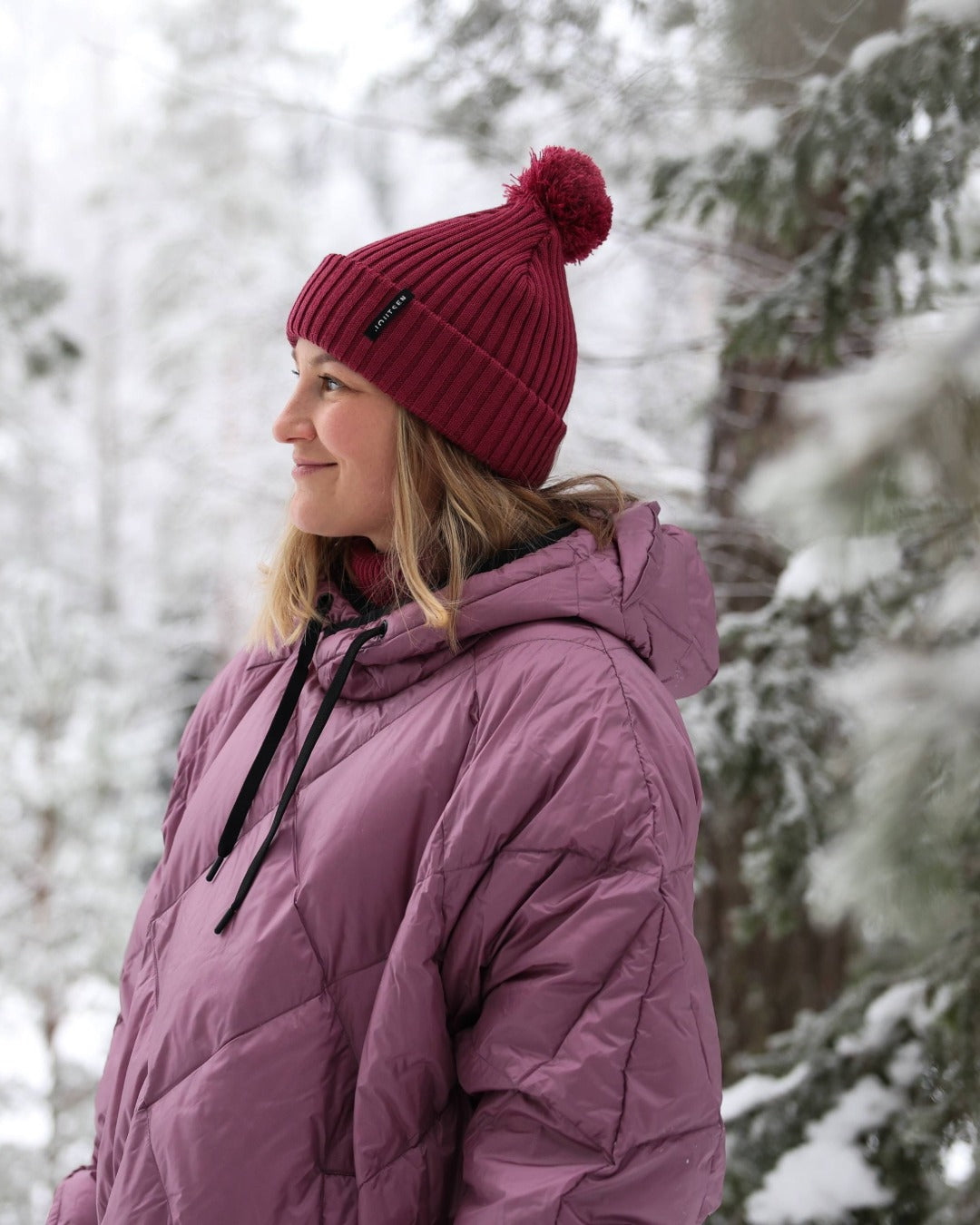Person wearing a light pink (color: Dusky orchid) down anorak and red beanie in a snowy forest
