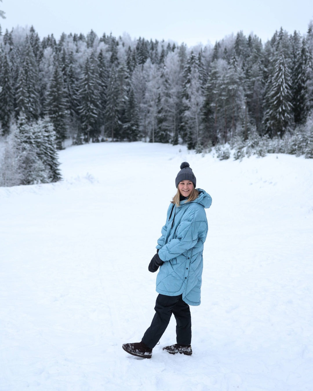 Person wearing a light blue down anorak standing in a snowy landscape with trees.