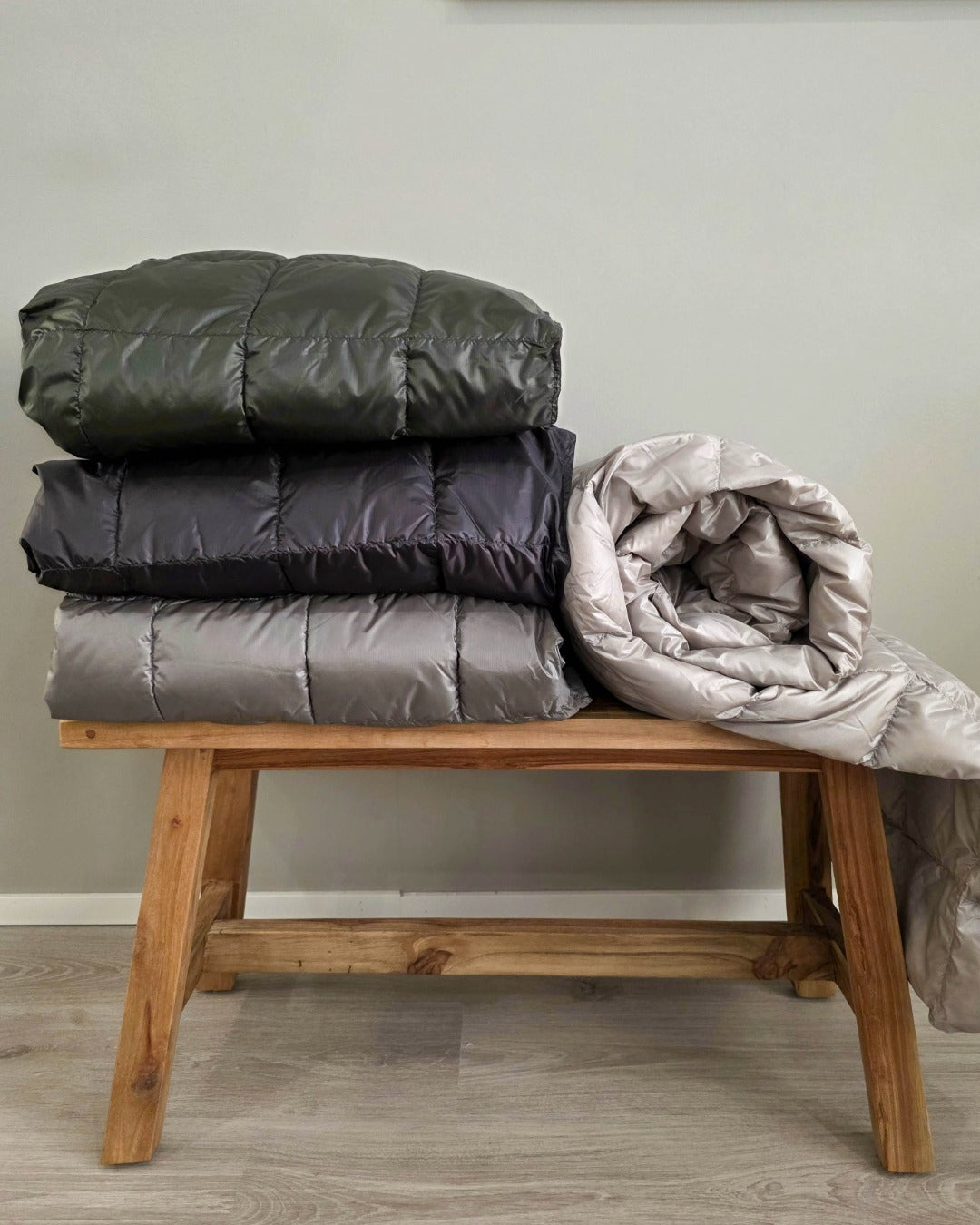 Four different Kulkuri down blankets on a wooden bench against a plain wall.