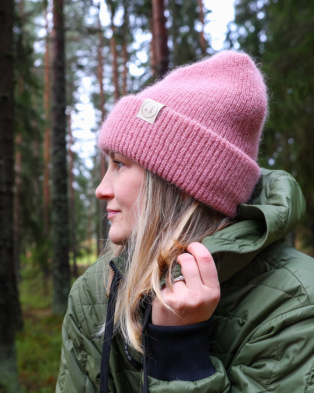 Person wearing a pink beanie and green jacket in a forest setting