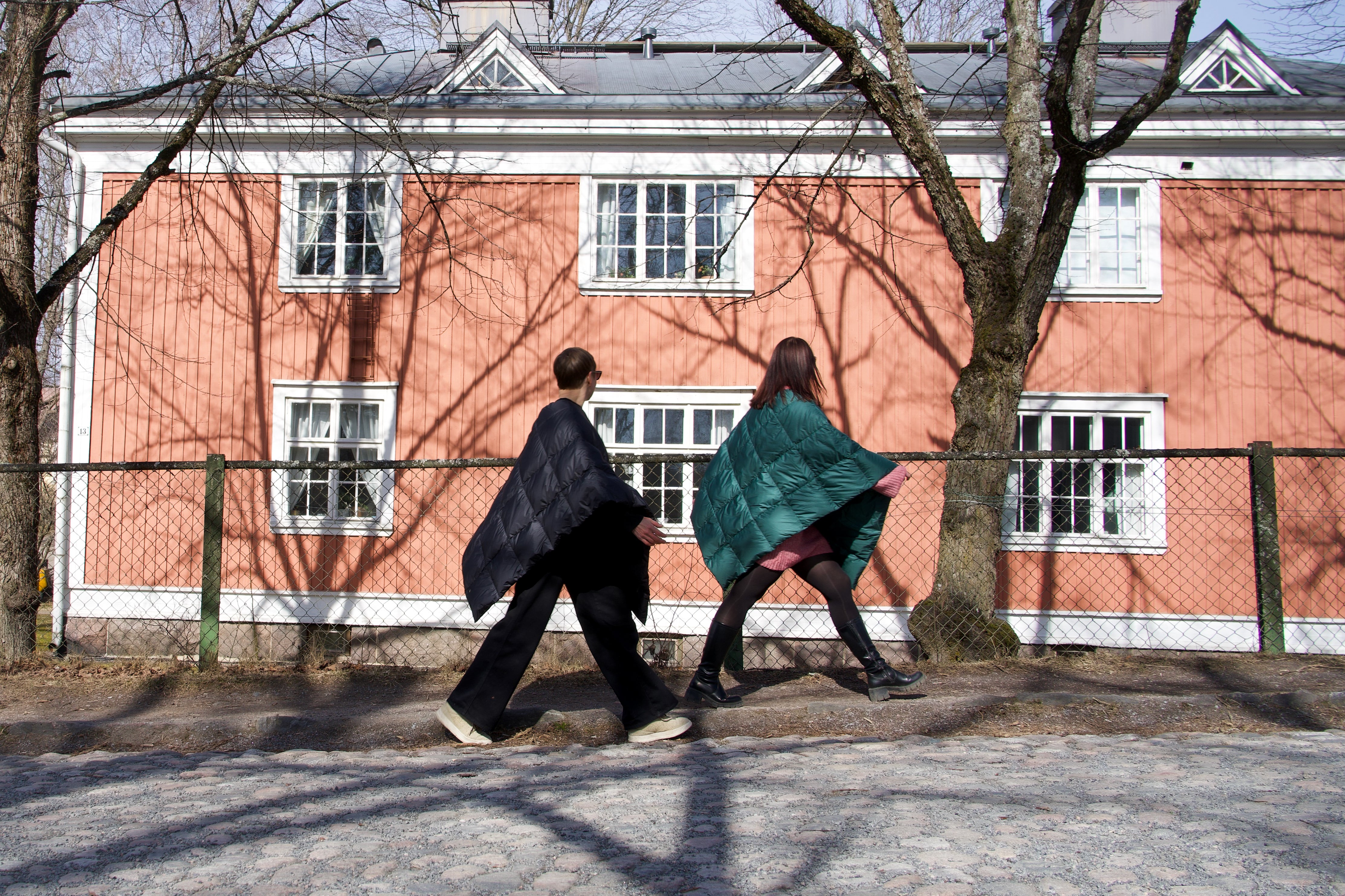 Two people are walking in the streets, one wearing a black Otava down poncho (color: charcoal black) and the other a green one (color: green paprika). 
