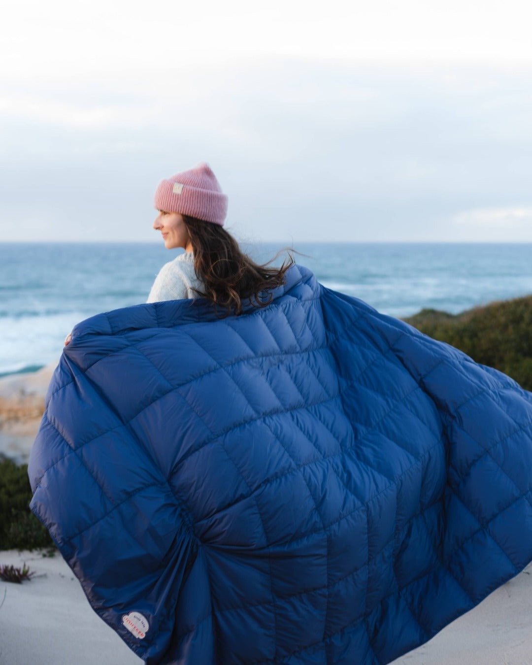 Person wrapped in a blue quilt with a scenic ocean view in the background