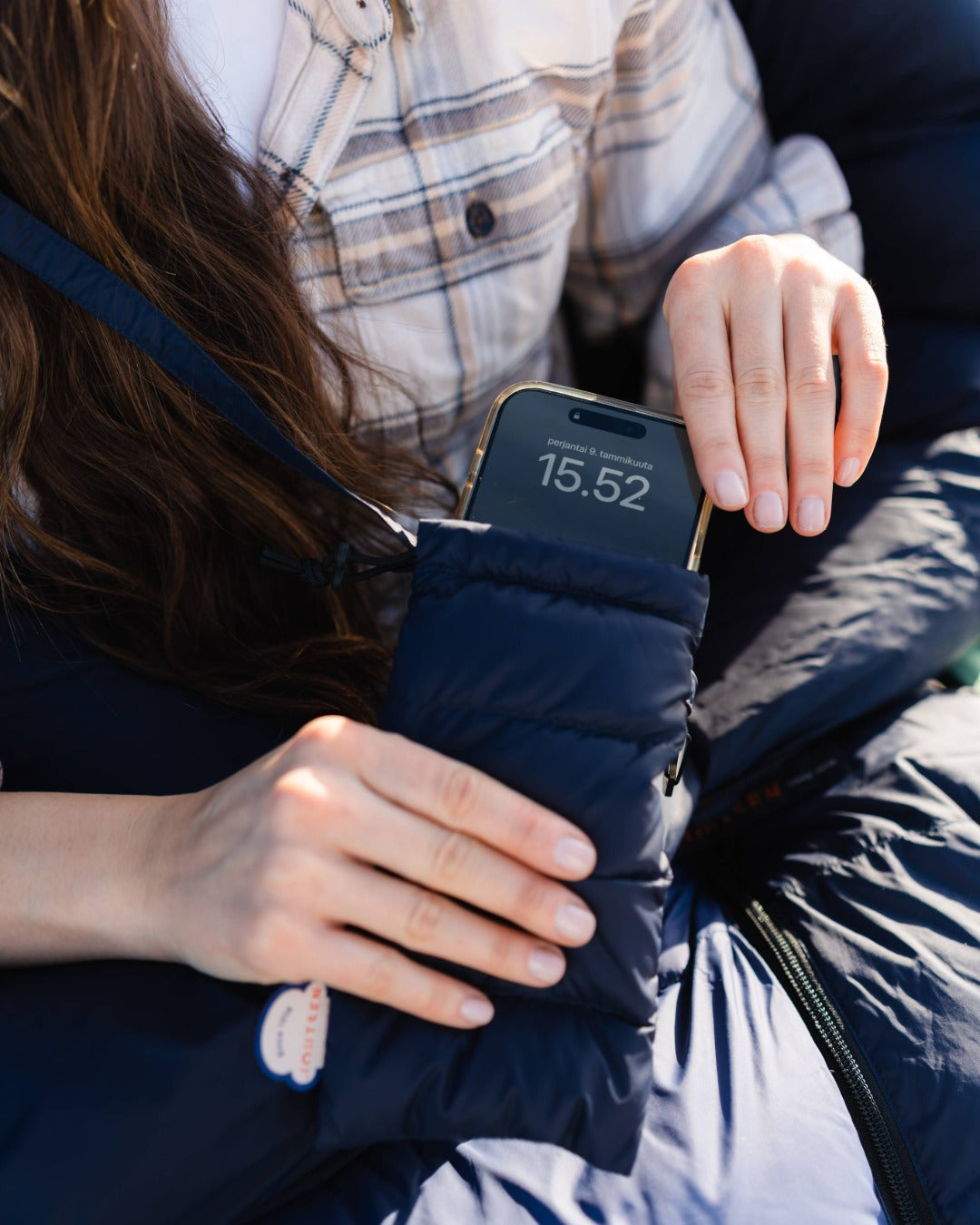 Person holding a phone pocket, wearing a plaid shirt and dark jacket.