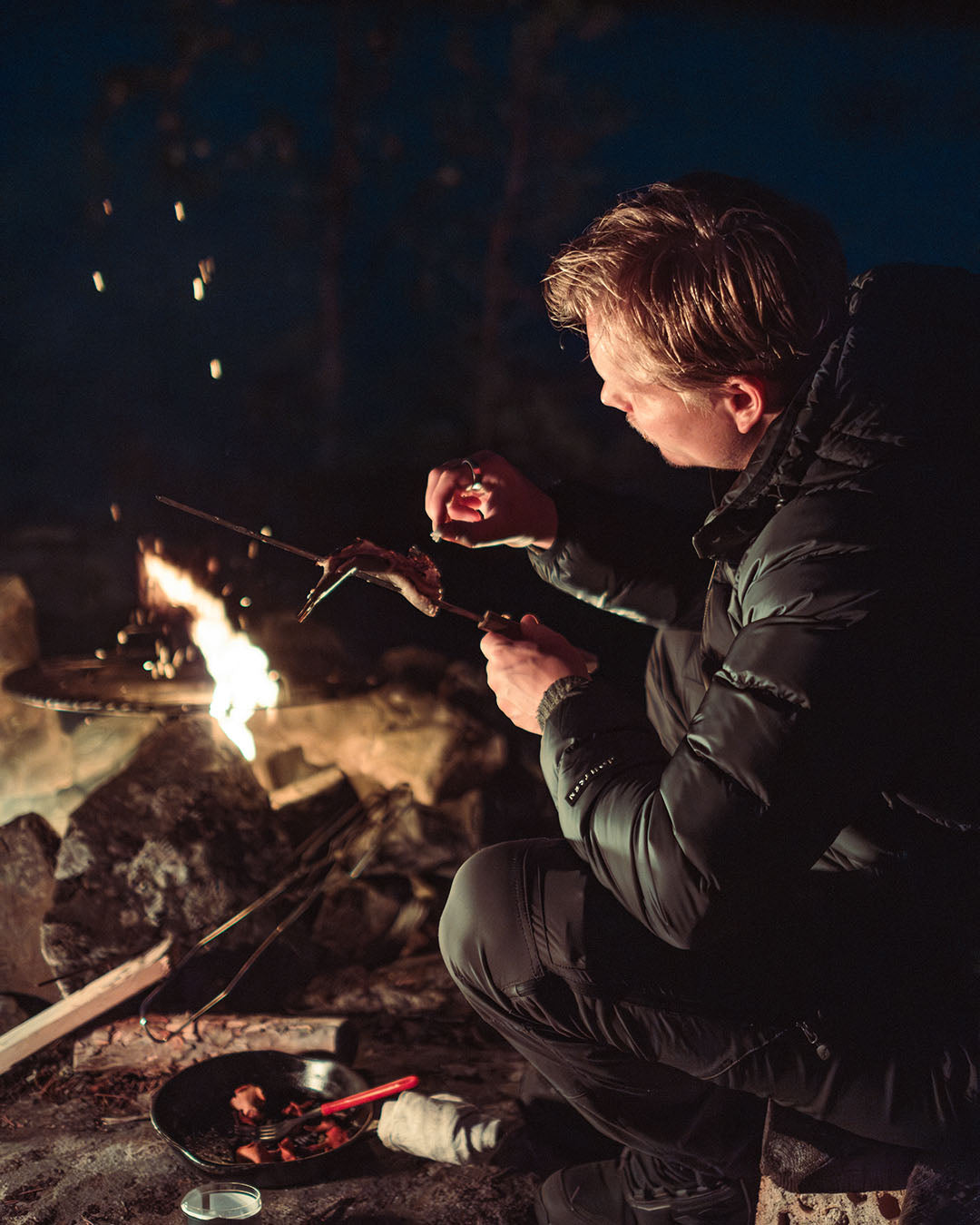 Person cooking over a campfire at night