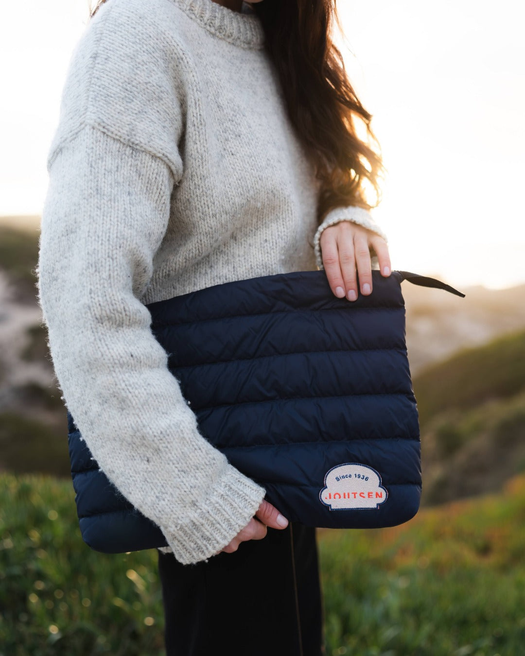 Person holding a navy blue down gear pouch with a logo in an outdoor setting
