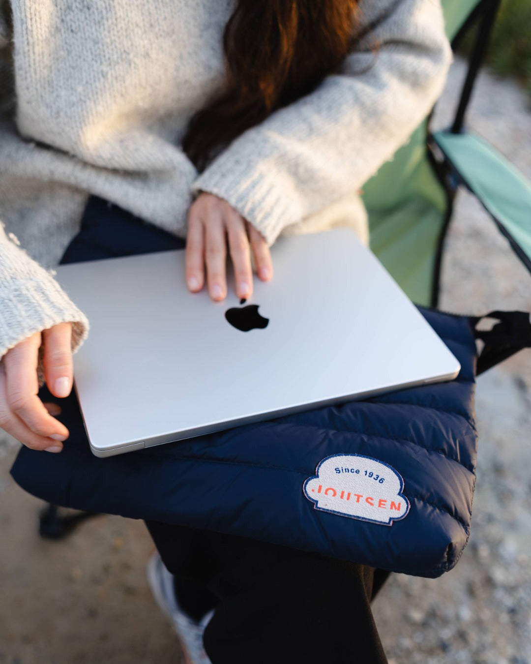 Person holding a laptop on a blue cushion with a visible brand logo.