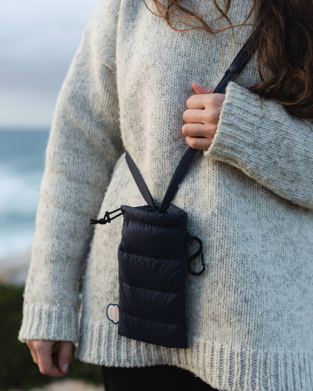 Person wearing a light gray sweater with a black drawstring pouch