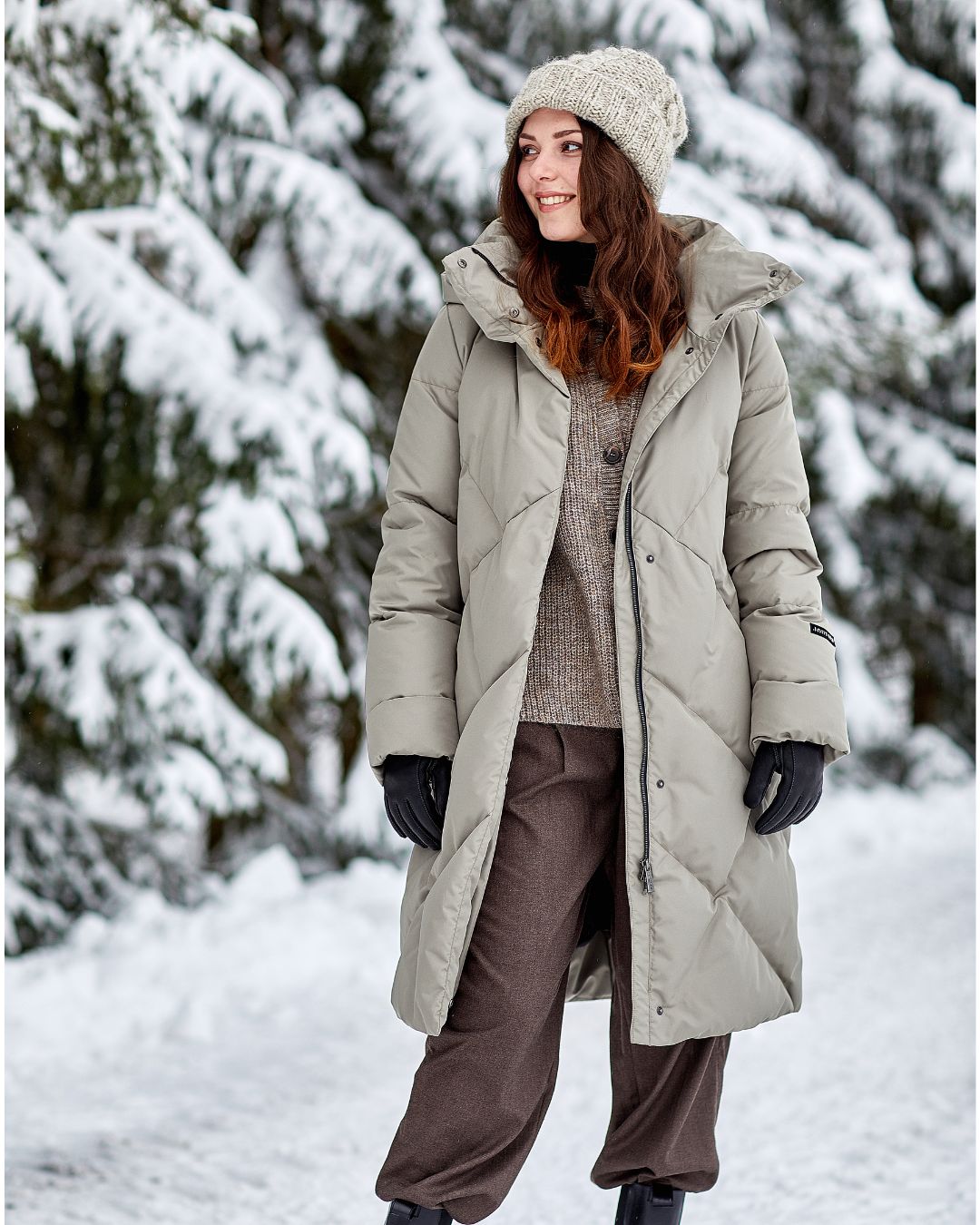 Woman in a long winter coat standing in a snowy landscape with trees.