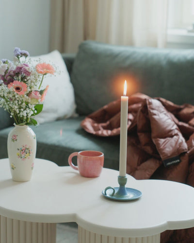 A woman is  laying down with brown (color: chocolate mousse) Kulkuri down blanket and having a cup of tea.