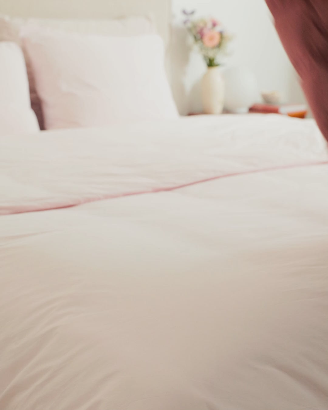 A light pink (color: old rose) Kulkuri down blanket is placed on a bed.